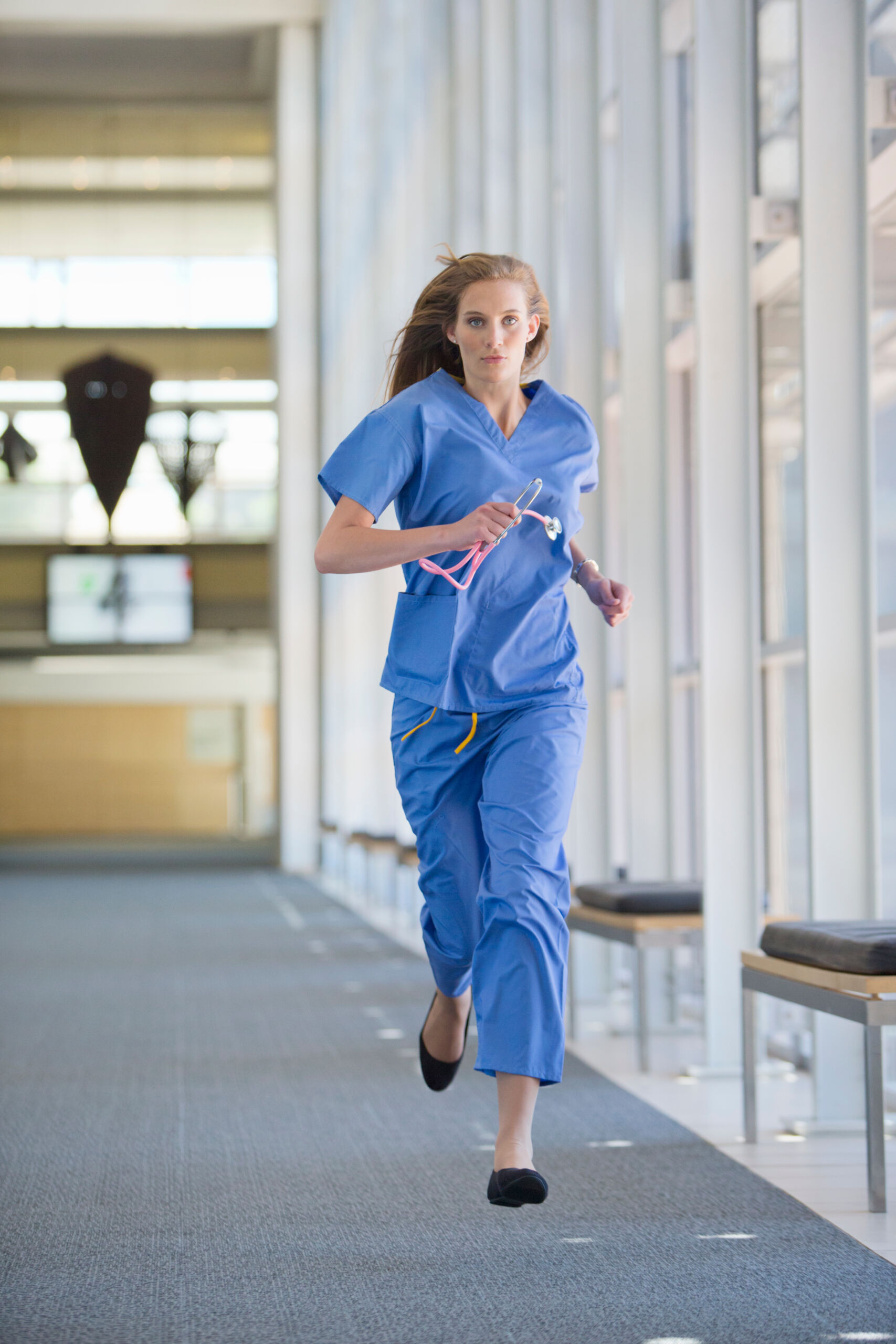 Healthcare professional walking confidently through a medical facility in blue scrubs.