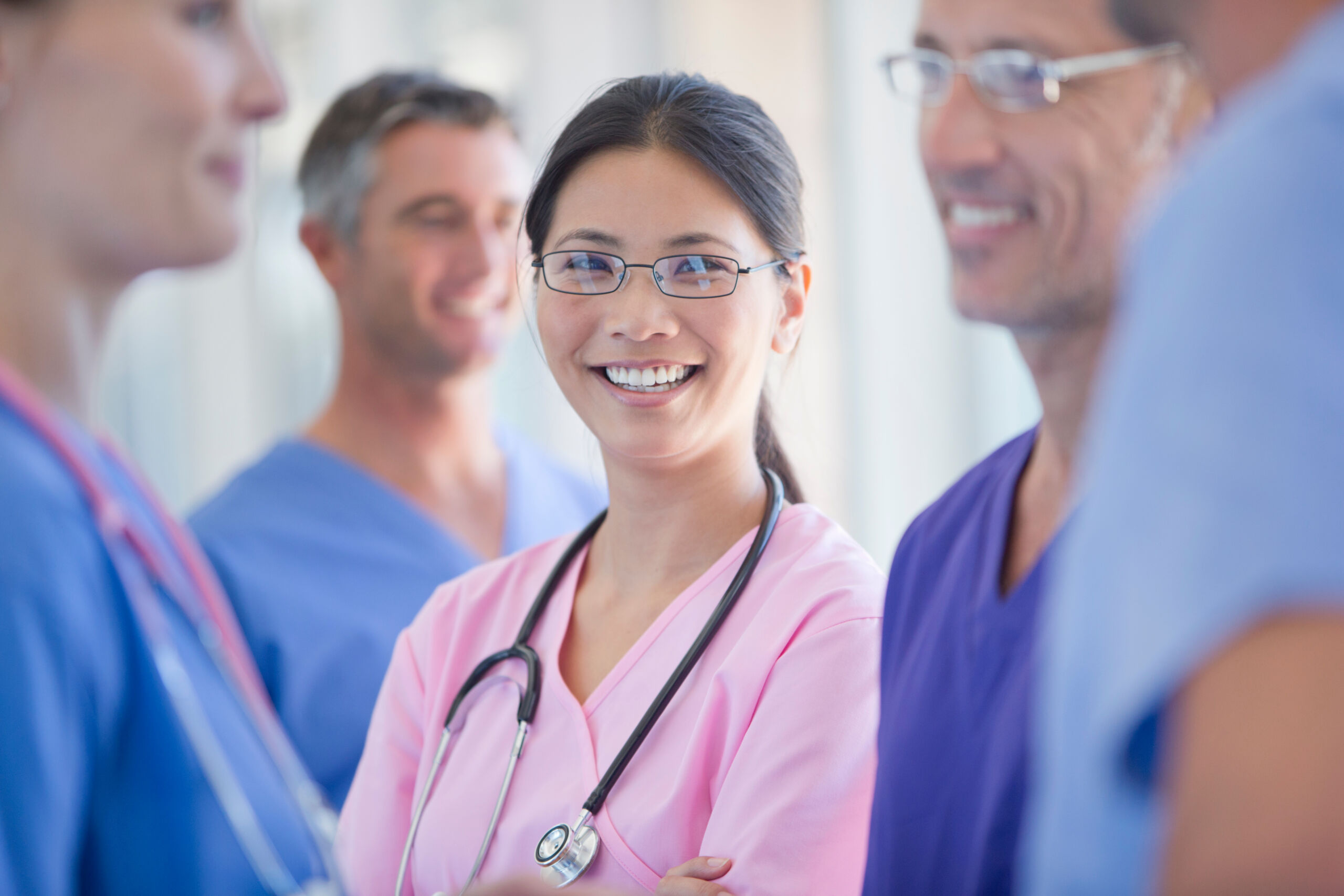 Healthcare worker in pink scrubs smiling in a hospital or clinic environment.